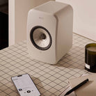 KEF LSX II LT Wireless HiFi Powered Bookshelf Speakers Stone White angled front view on countertop with cell phone