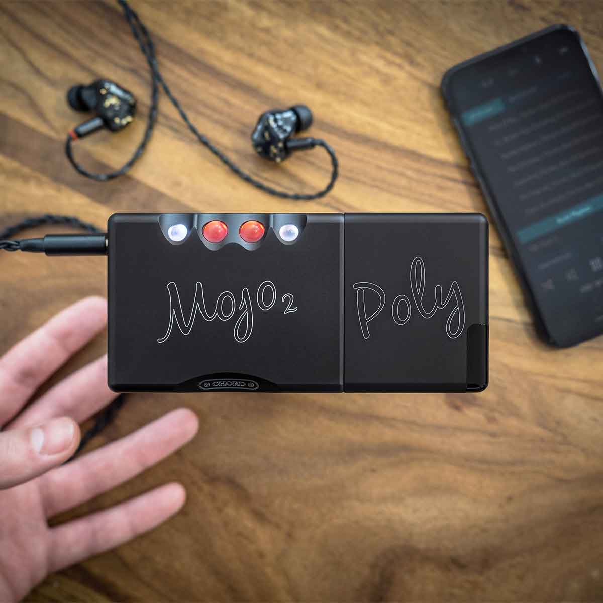 Chord Mojo 2 is attached to Chord Poly music streamer with a pair of in-ear headphones and a smartphone in the background.