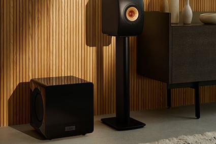 KEF KC92 Subwoofer in black on the floor beside a speaker on a stand