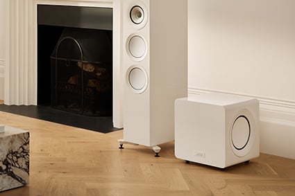 KEF KC92 Subwoofer in white next to a white tower speaker in a living room