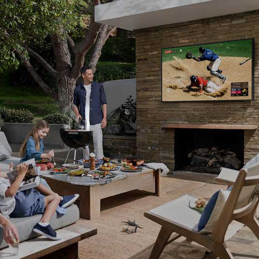 Family having a cookout on a patio while watching baseball on an outdoor tv