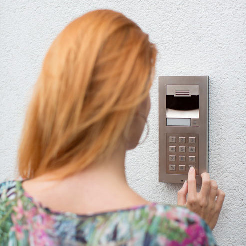 Back view of a red haired woman with her finger on security panel on the wall