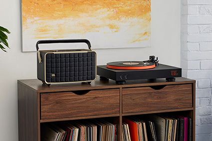 JBL Spinner BT Bluetooth Turntable in orange next to a retro speaker