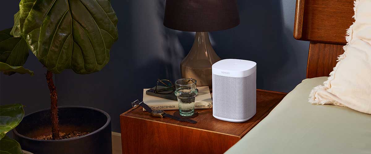 A portable speaker on a night stand beside a bed