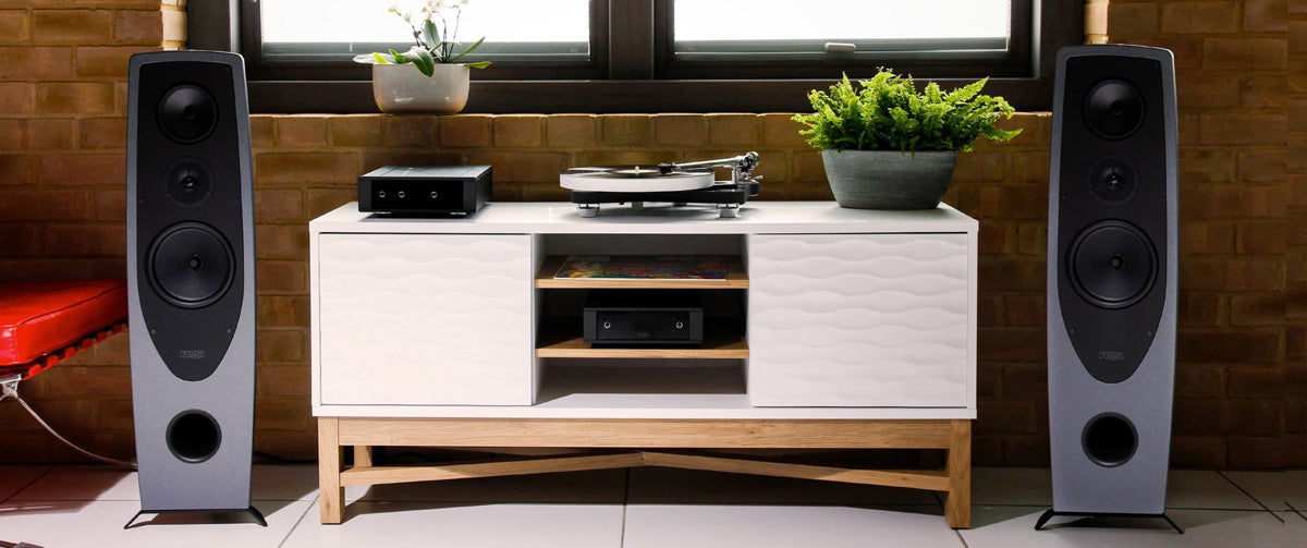 Rega AYA Loudspeakers on either side of a console cabinet in front of a window