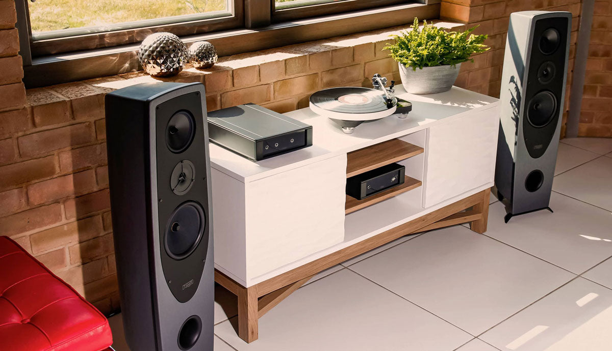 3/4 view of Rega AYA Loudspeakers on either side of a console cabinet in front of a window